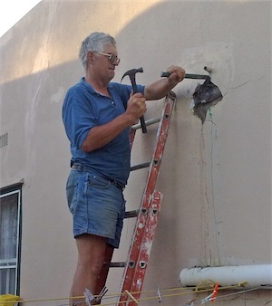 A handyman uses a hammer and chisel to open a hole into the wall so that he can repair a leaking pipe